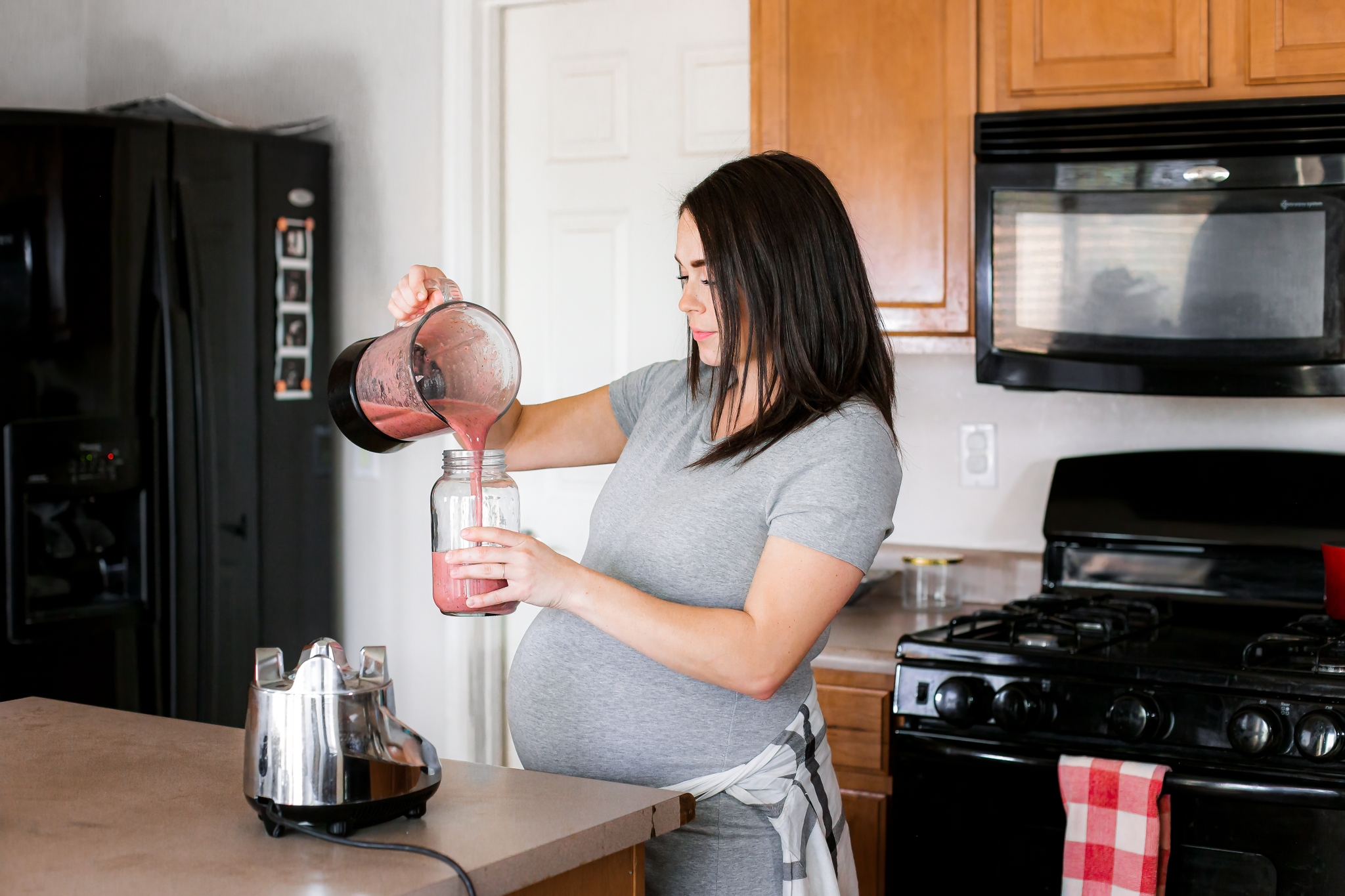 Foods to avoid when pregnant: Woman with pronounced baby bump is in kitchen pouring herself a beverage