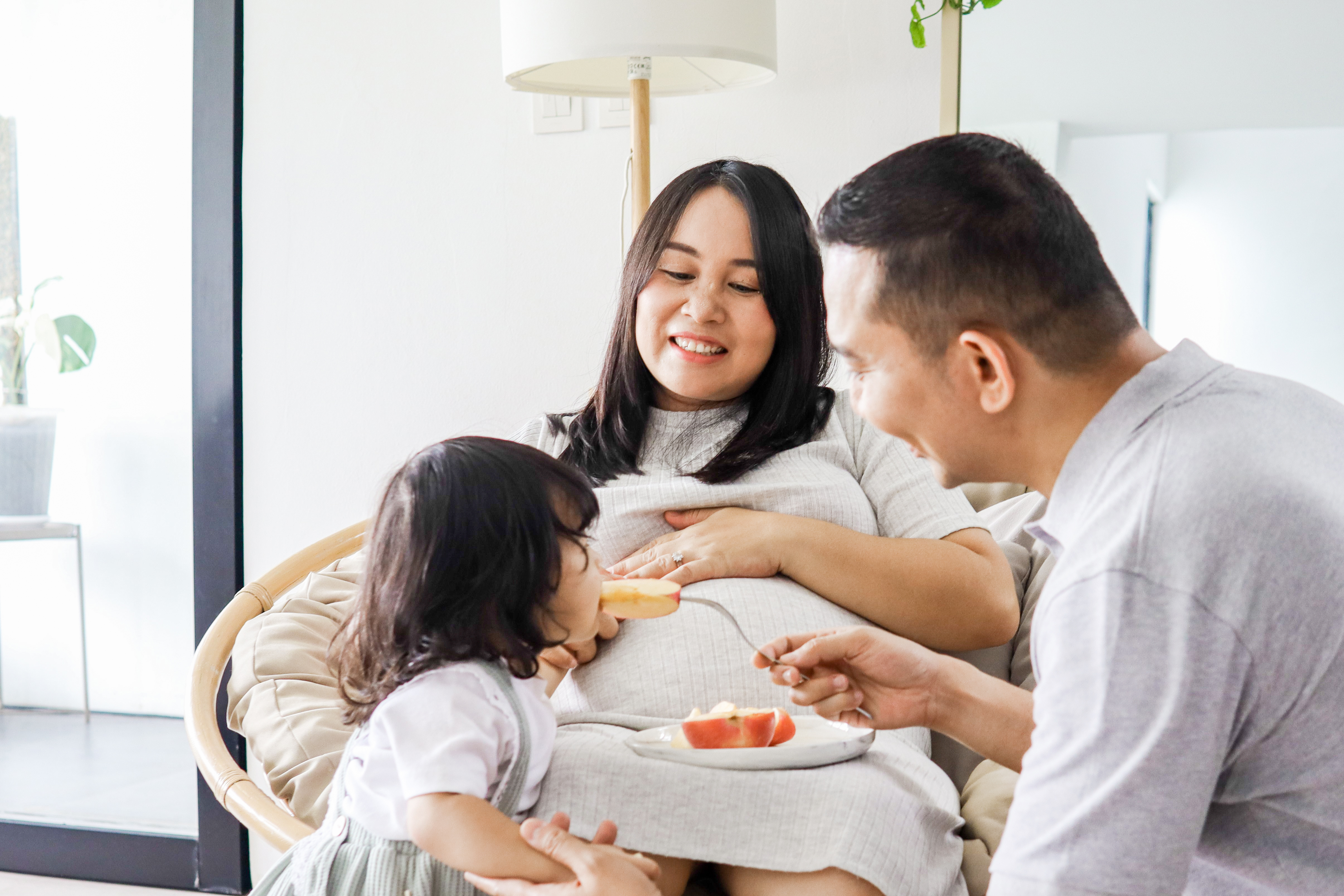 Foods to avoid when pregnant: Pregnant mom, dad, and daughter eat a snack together